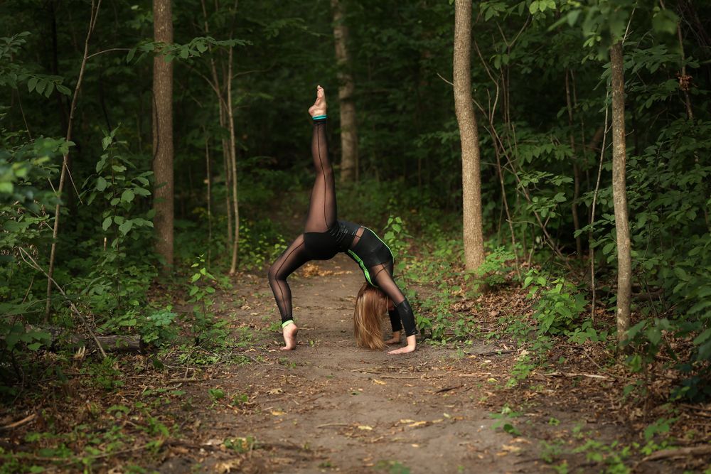Graceful dancer performing backbend on forest path wearing black leotard.