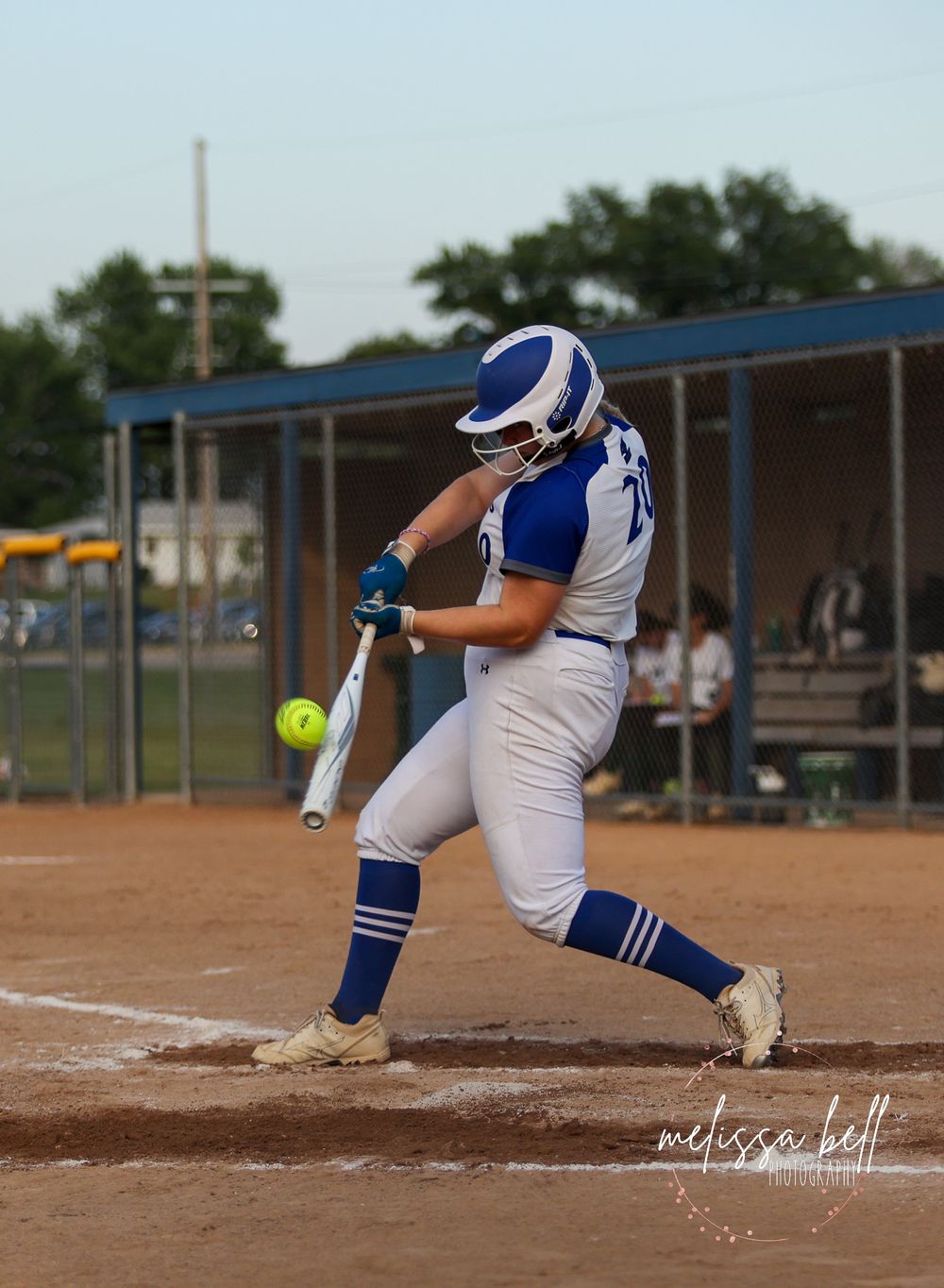 Softball batter in white and blue uniform preparing to hit incoming pitch.