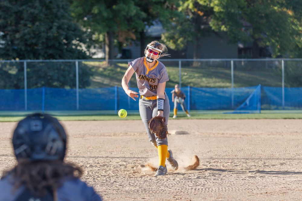 Softball pitcher in mid-delivery motion throwing a pitch on a dirt field.