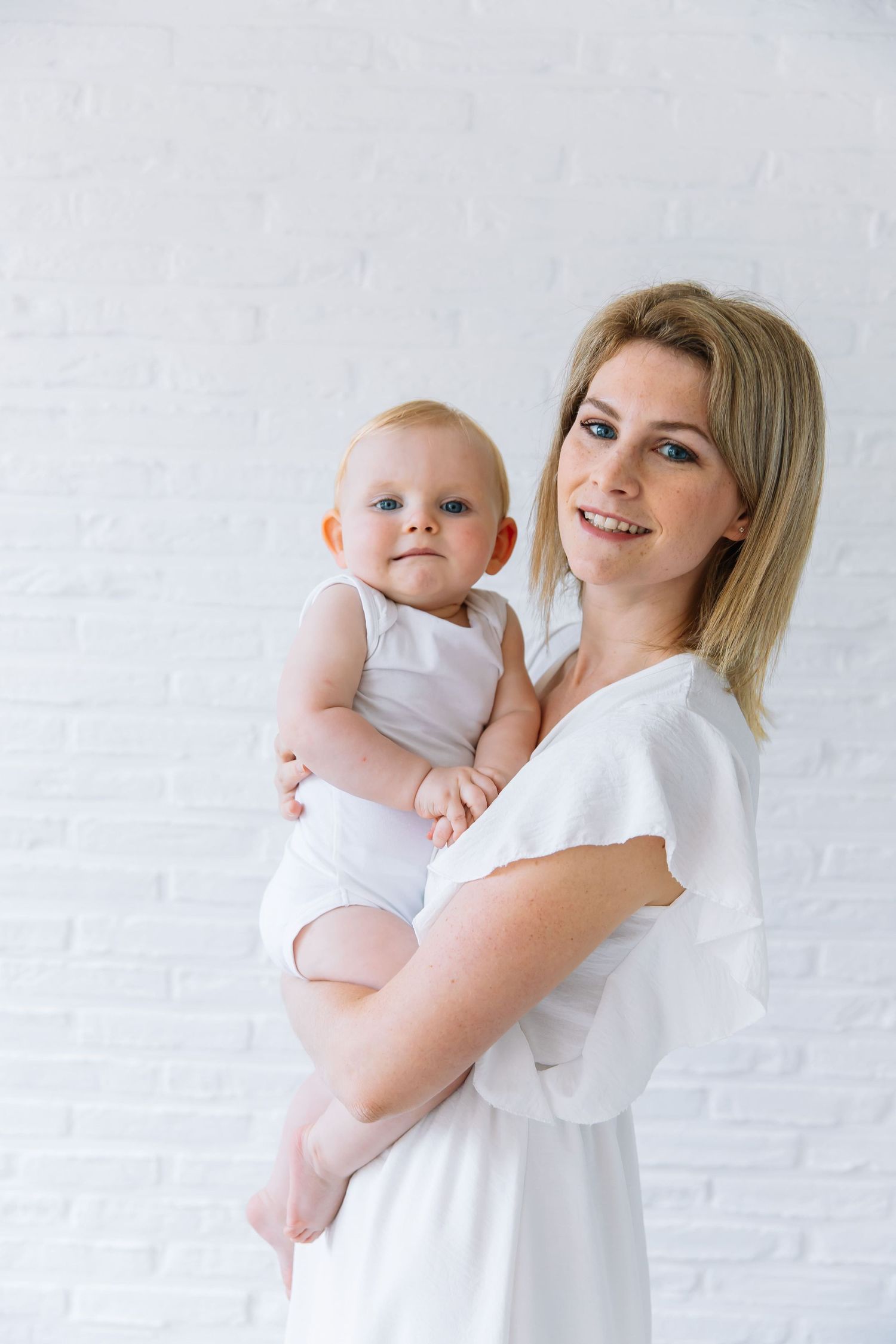 A tender moment between parent and baby in white outfits against a light background.