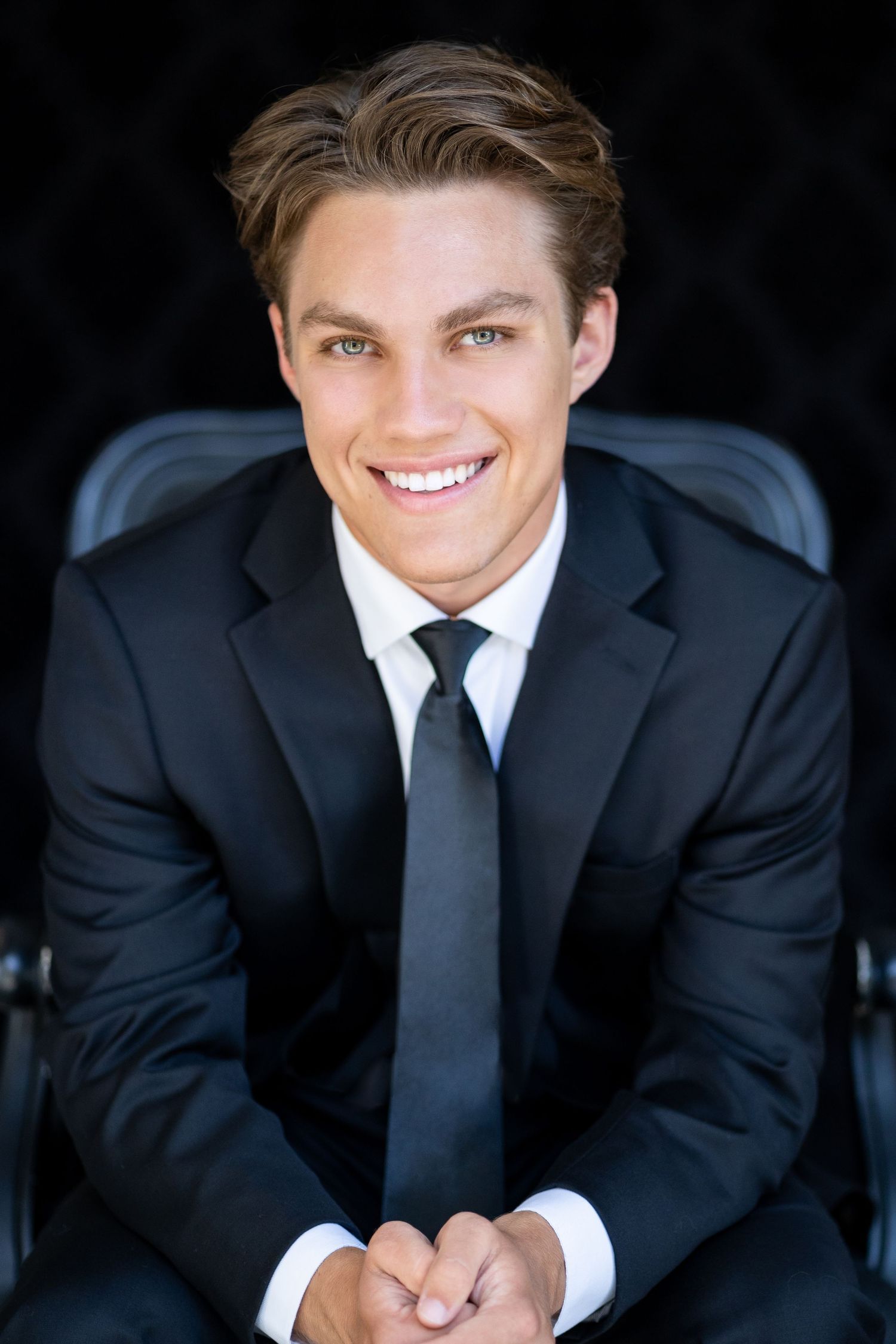 Professional headshot of a high school senior in black suit and tie with bright smile.