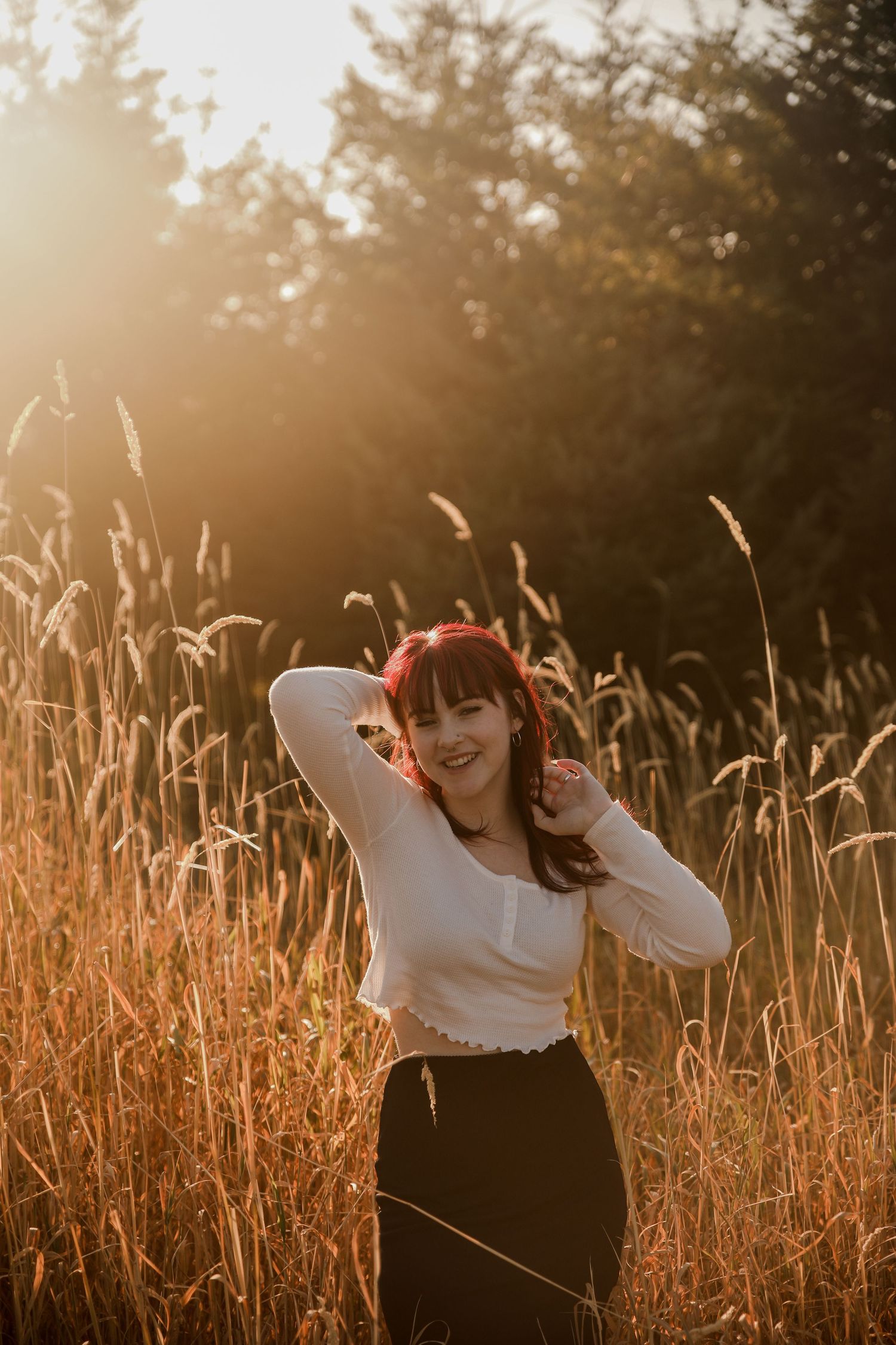Person in white top and dark skirt posing playfully in a golden wheat field at sunset.