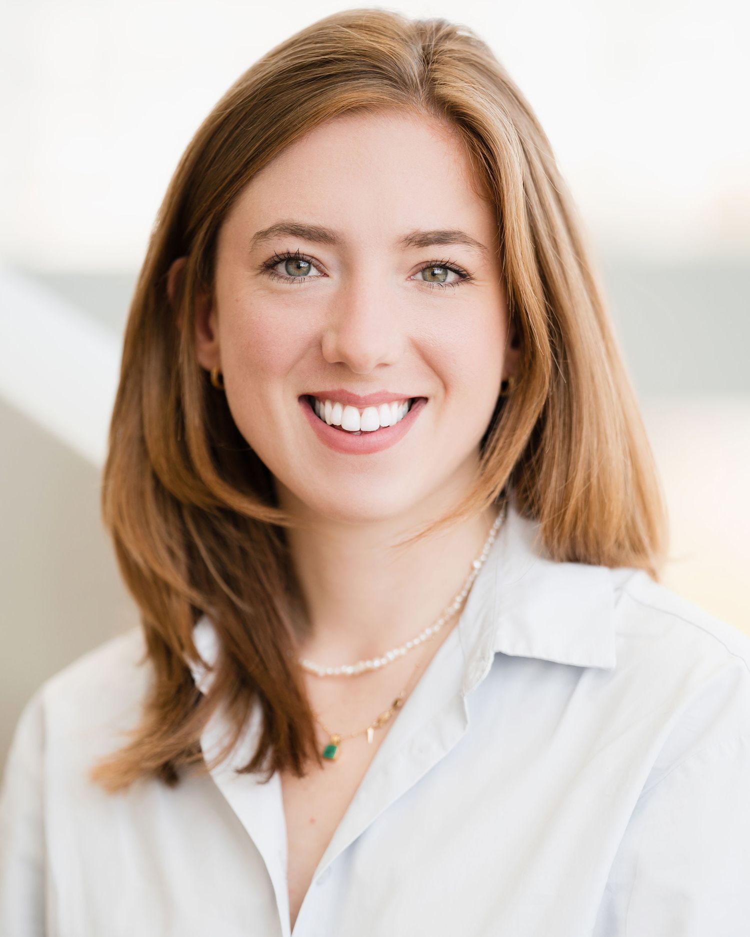 Professional headshot of someone in a white blouse with a bright smile.