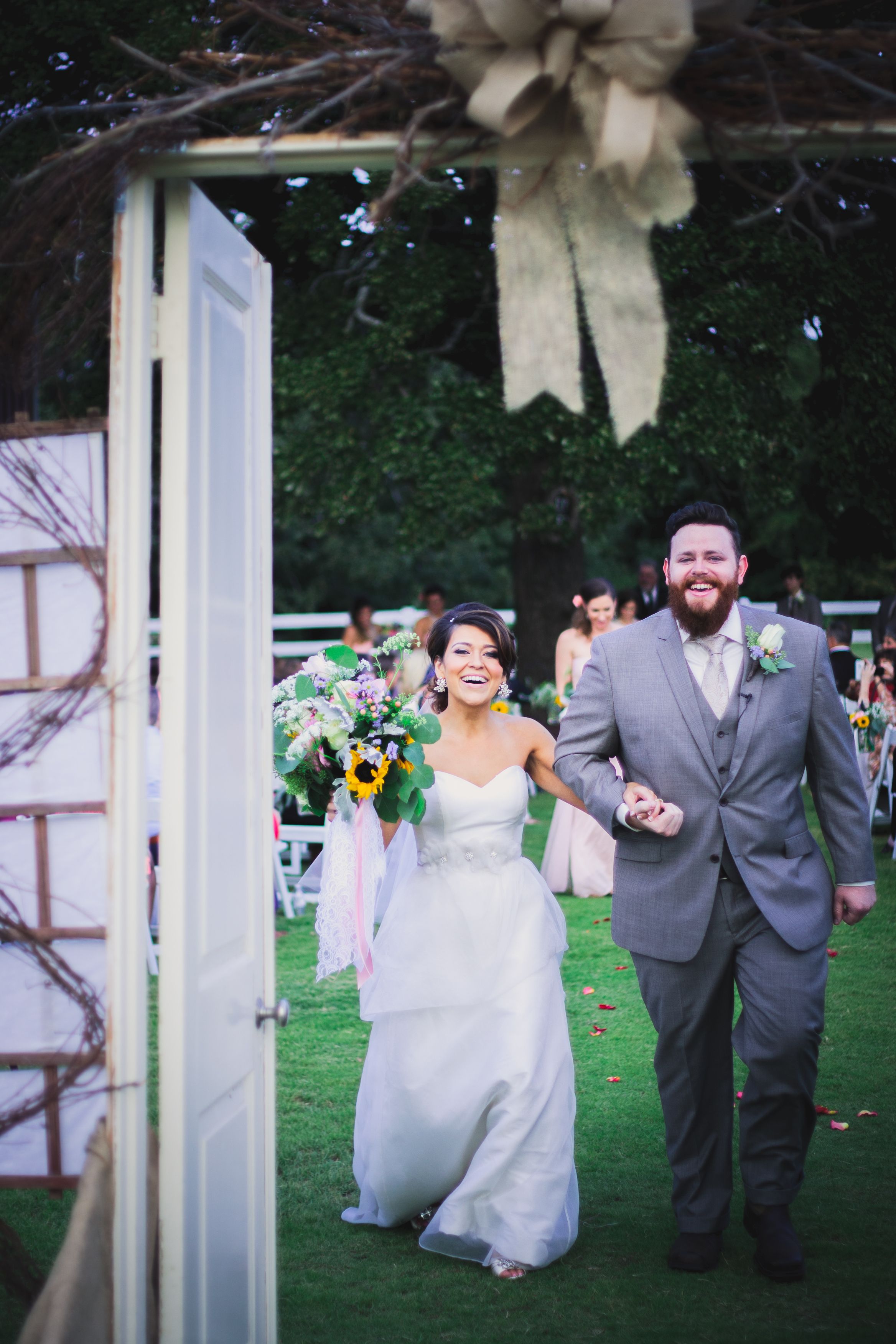 A joyful couple exits through decorated doors into a garden wedding reception.