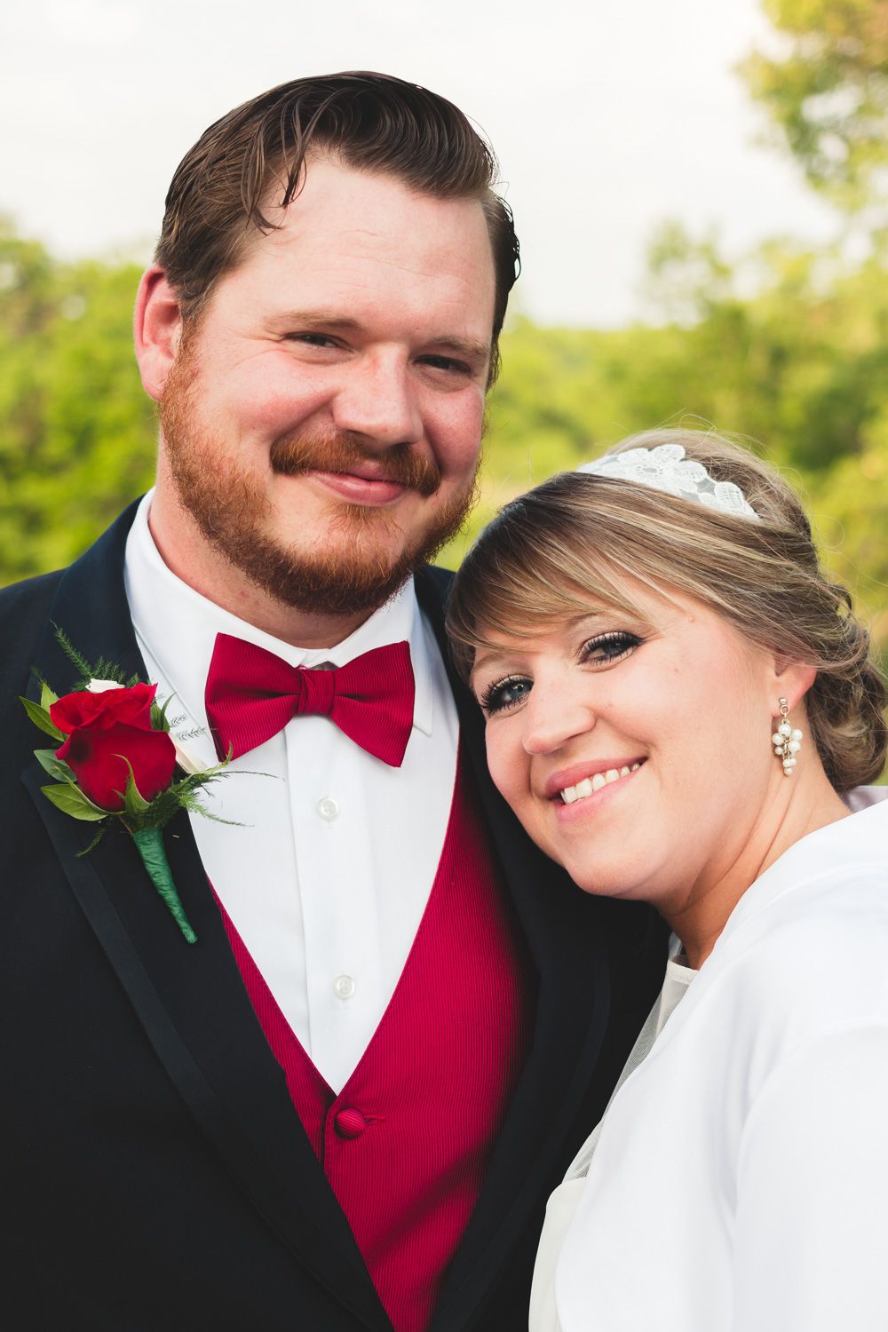 A formal wedding portrait featuring red bow tie and boutonniere details.