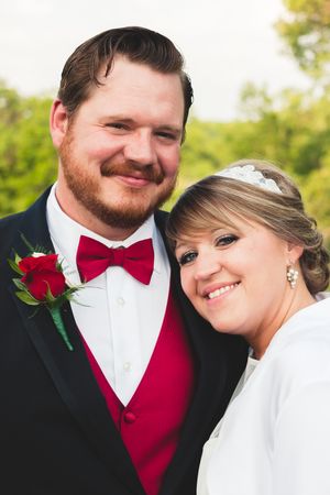 A formal wedding portrait featuring red bow tie and boutonniere details.