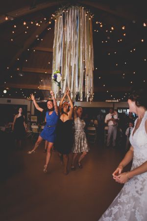 Wedding guests reach for a bouquet toss under hanging streamers and string lights.