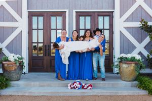 Wedding party members hold a banner while standing on the steps of a rustic barn with blue doors.