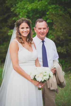 A bride in white dress holds bouquet while posing outdoors.