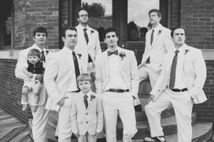 Groomsmen in white suits pose casually on brick steps.