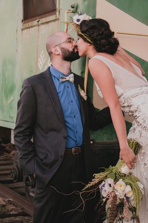 Romantic portrait of newlyweds kissing near a vintage green train car.