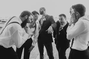 Black and white photo of groomsmen sharing a candid moment in formal attire.