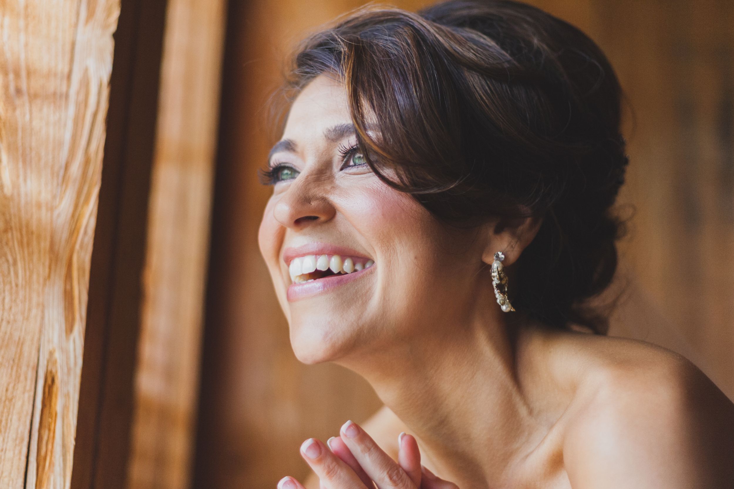Natural light portrait of someone smiling by a window with elegant hairstyling.