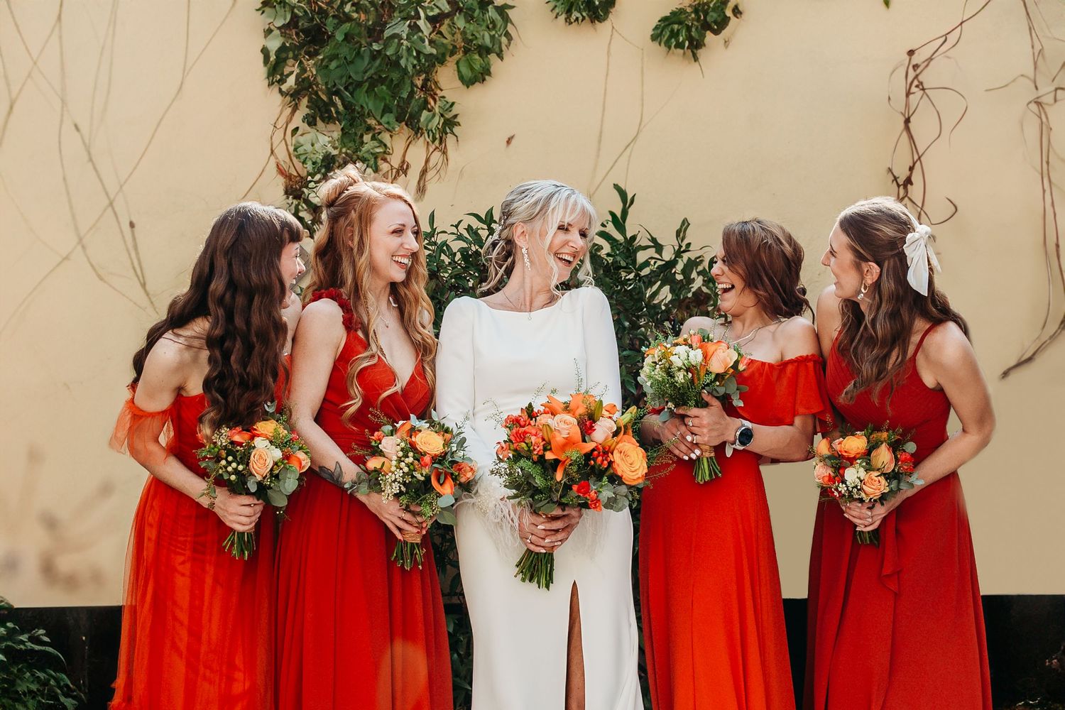 Wedding party in red bridesmaid dresses with colorful autumn bouquets.