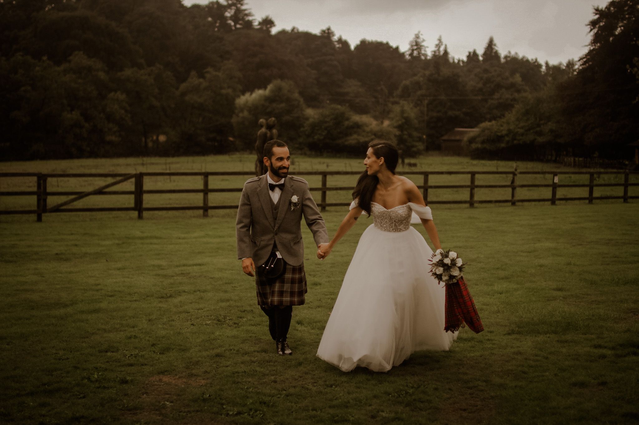Wedding group walking together across expansive lawn at countryside estate.