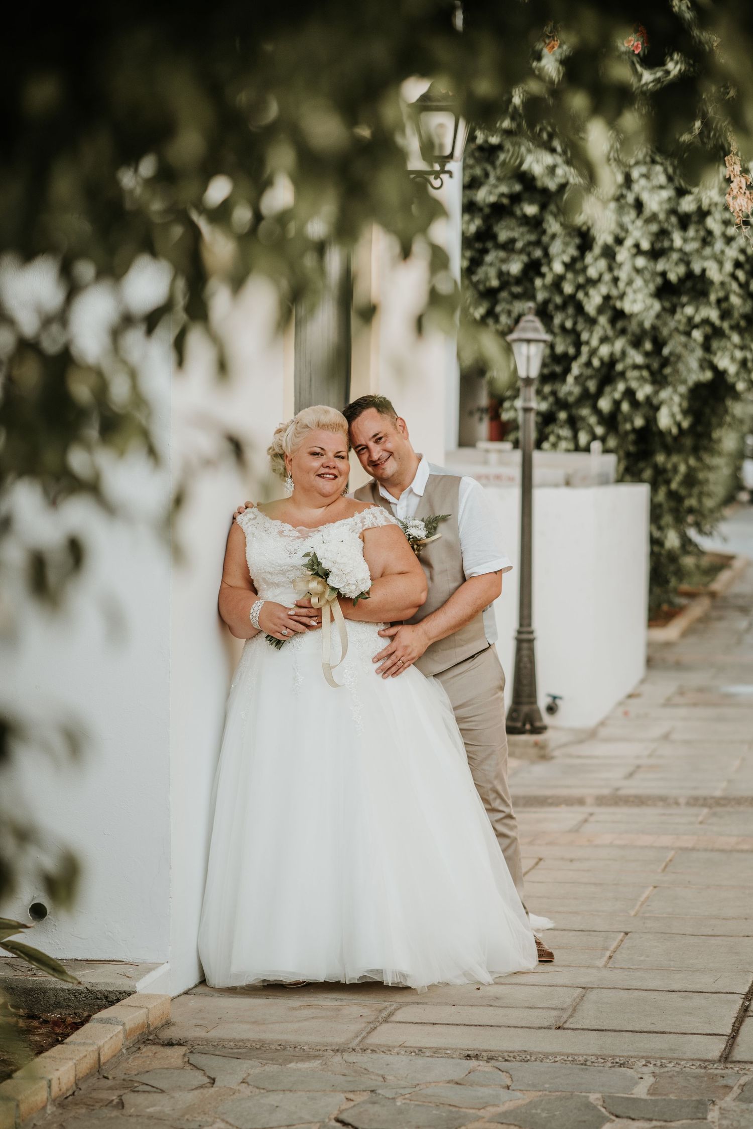 Intimate wedding couple portrait under leafy garden archway with romantic lighting and stone pathway.