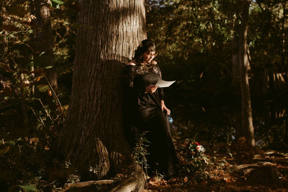 Person reads intently while leaning against a large tree trunk in a sunlit autumn forest.