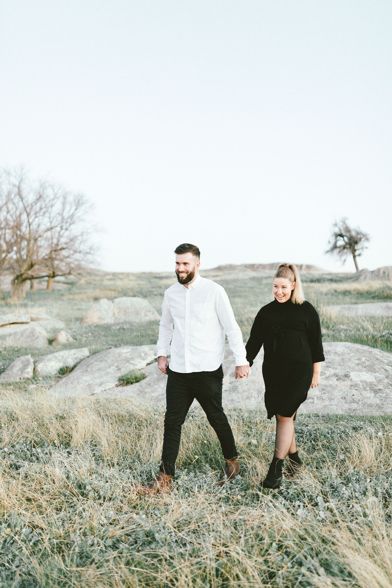 Couple walking together on rocky terrain with sparse vegetation.