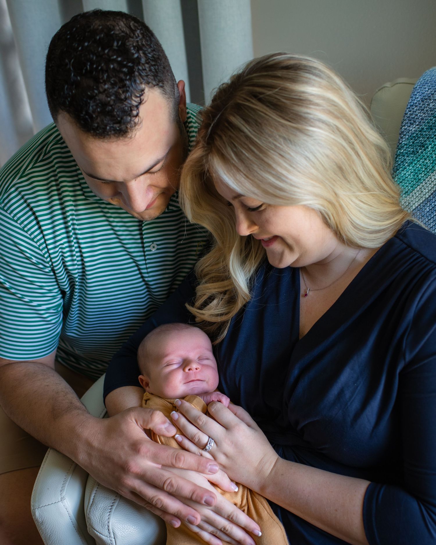 New parents holding their newborn baby while sitting in a cozy chair.