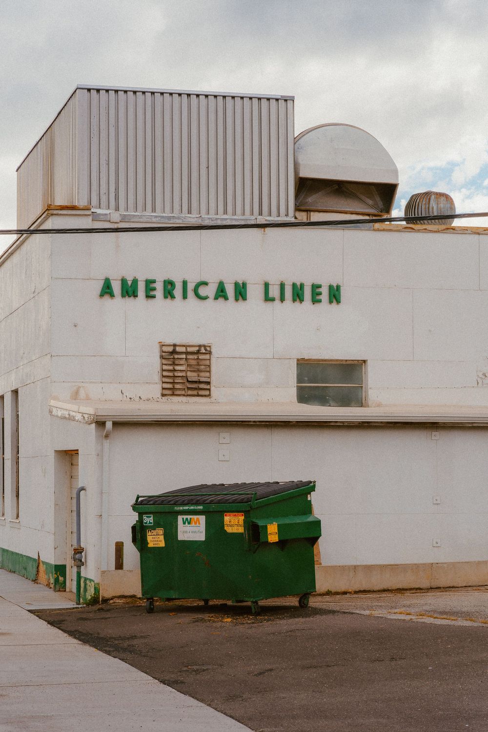 White industrial building with American Linen signage and a green dumpster.