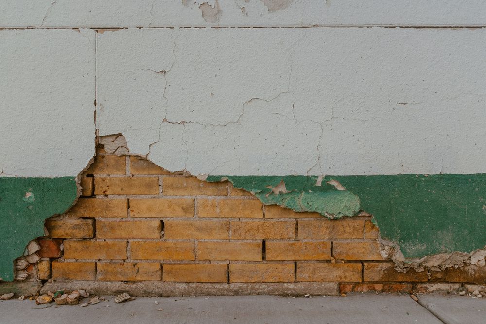 Exposed brick wall showing through damaged plaster with white and green paint sections.