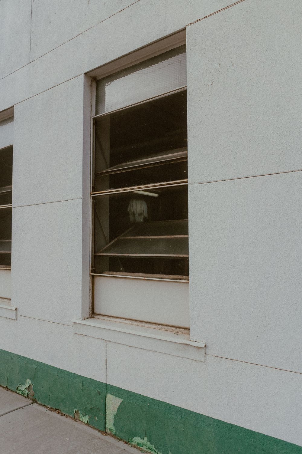 Open window on white industrial building wall with green trim.