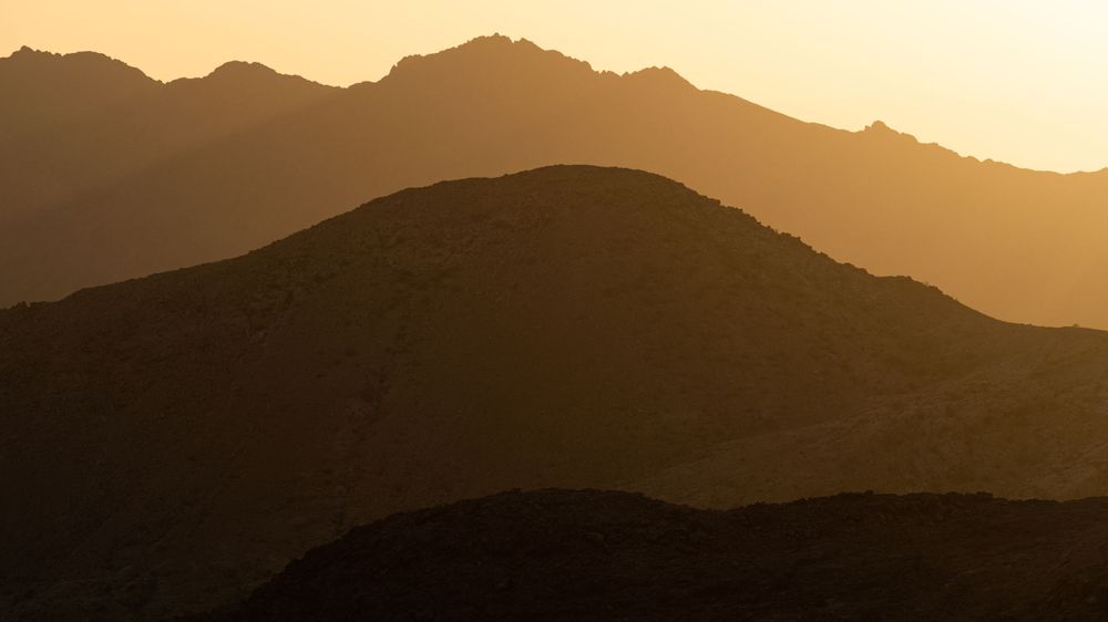 Silhouetted mountain ranges at sunset creating layers of dark ridges against golden sky.