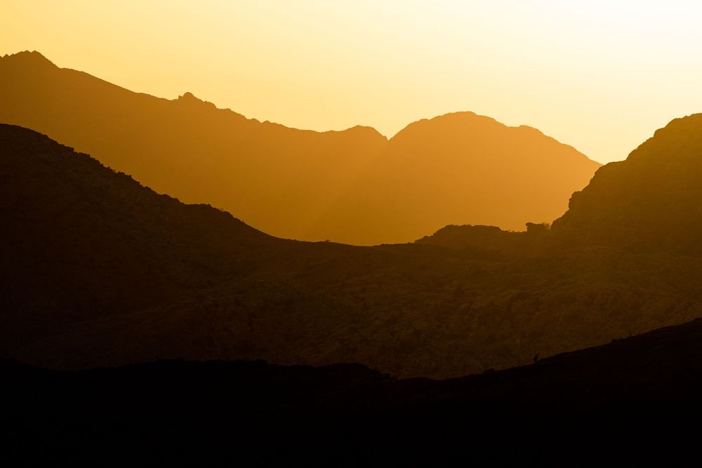 Dramatic mountain silhouettes against warm golden sunset sky in desert landscape.
