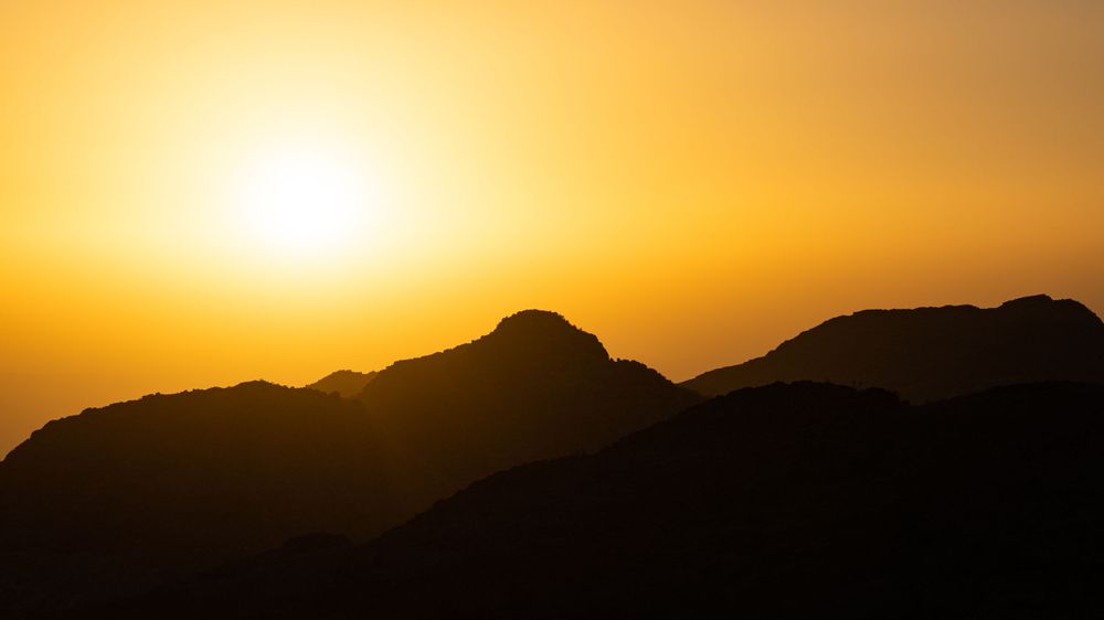 Golden desert sunrise over dark mountain silhouettes creating dramatic morning landscape.