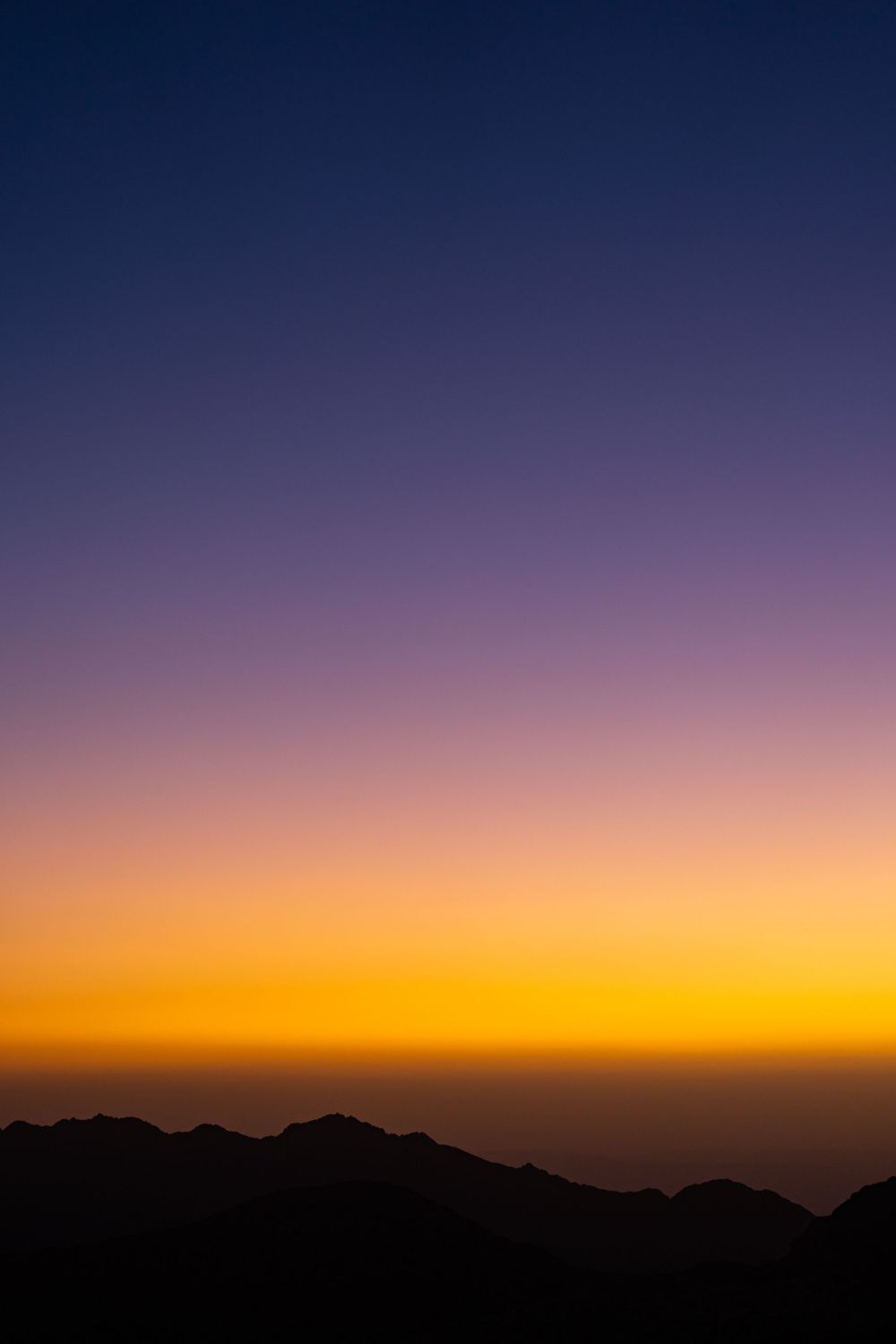 Mountain silhouettes against a gradient sky transitioning from dark blue to orange at sunset.