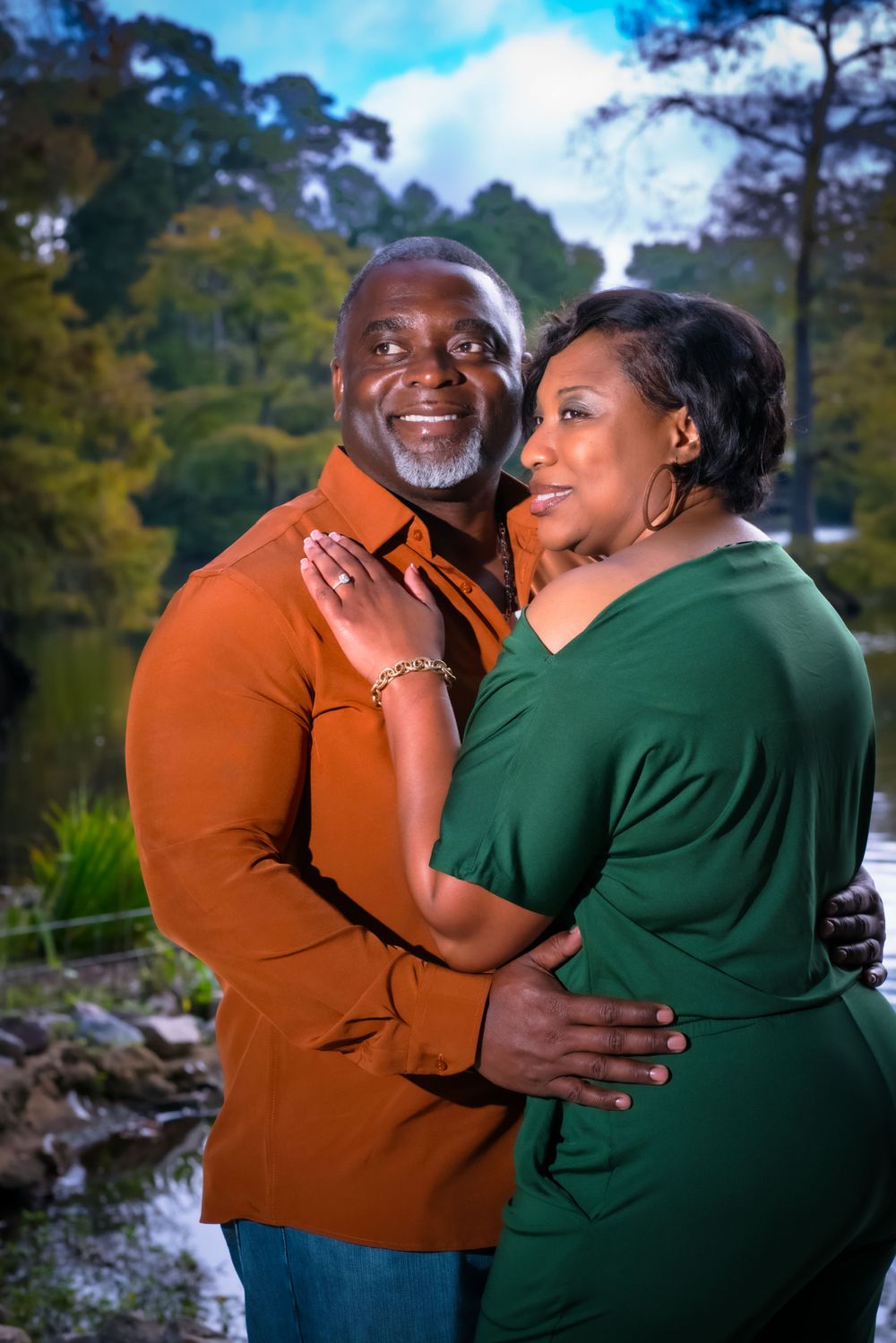 A couple in coordinated orange and green outfits pose together in a romantic outdoor setting.