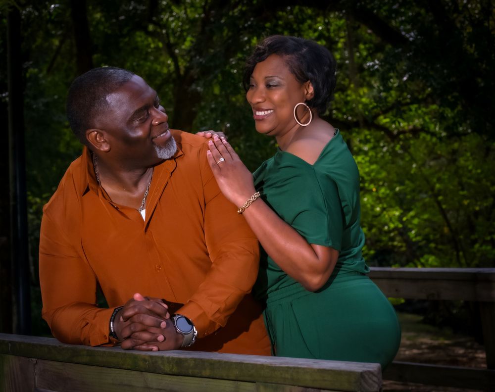 A couple dressed in orange and green share a laughing moment together on a wooden bench.