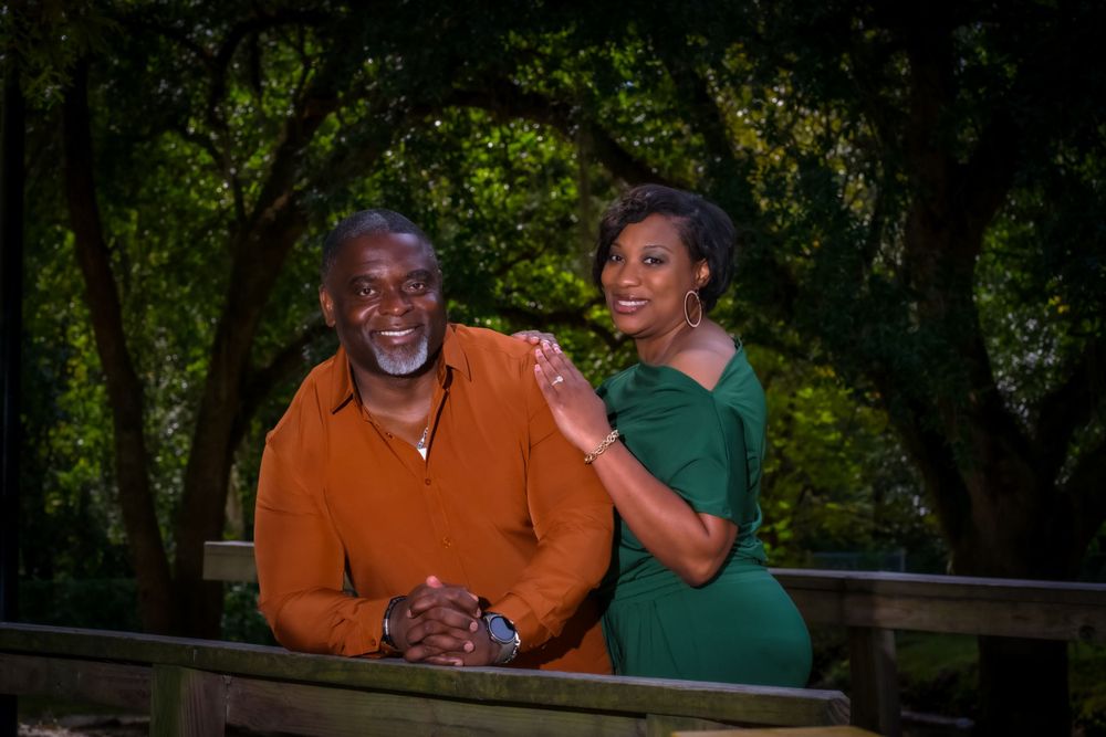 A couple in orange and green outfits sharing a joyful moment outdoors in a natural setting.