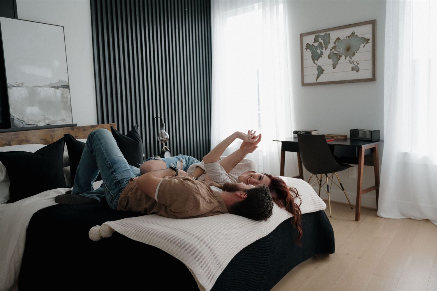 Two people laying on a bed in a modern bedroom with minimalist decor and world map art.