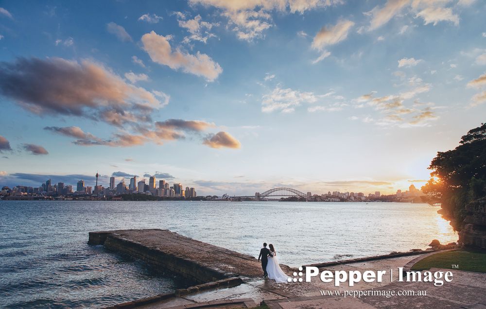 Wedding couple on dock with stunning Sydney Harbour Bridge and city skyline at sunset.