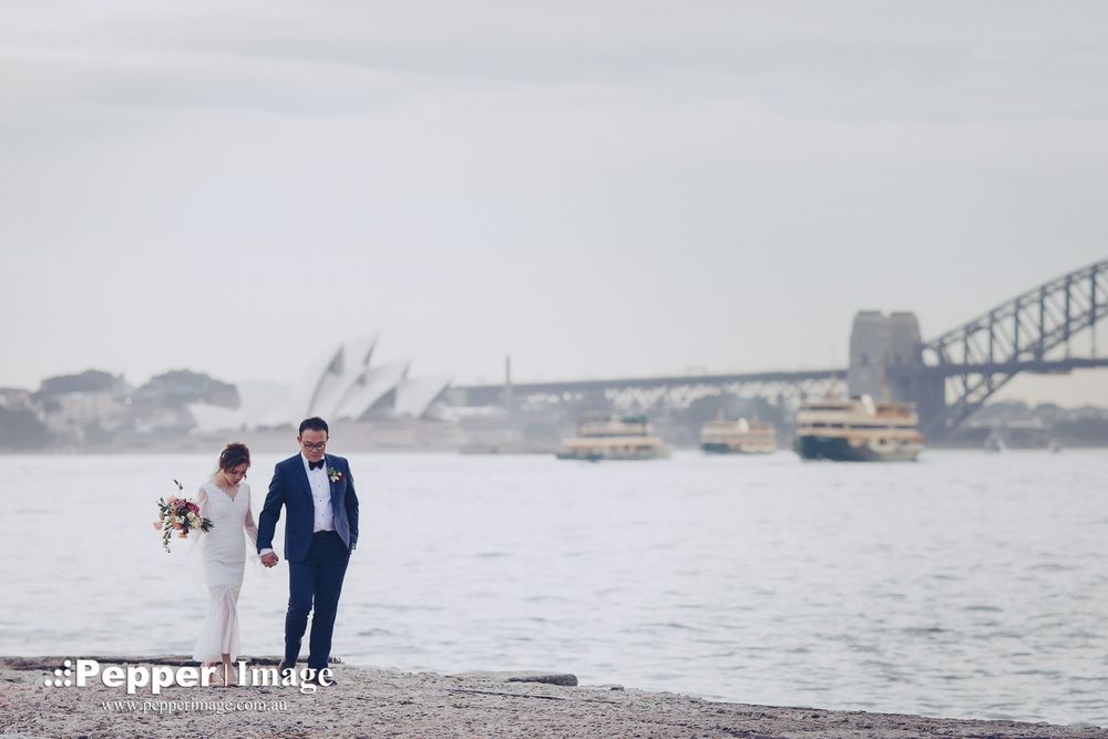 Bride and groom walking on Sydney Harbour foreshore with Opera House and Bridge behind.