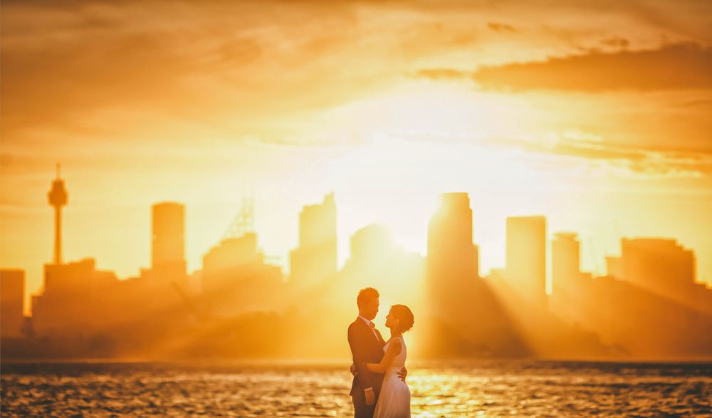 Romantic wedding couple silhouetted against golden Sydney city skyline at sunset.