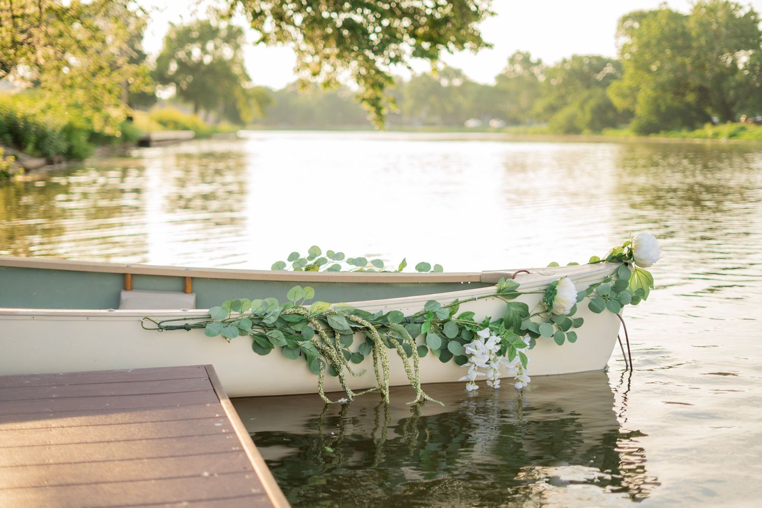 White canoe decorated with greenery garland docked on a calm river at golden hour.