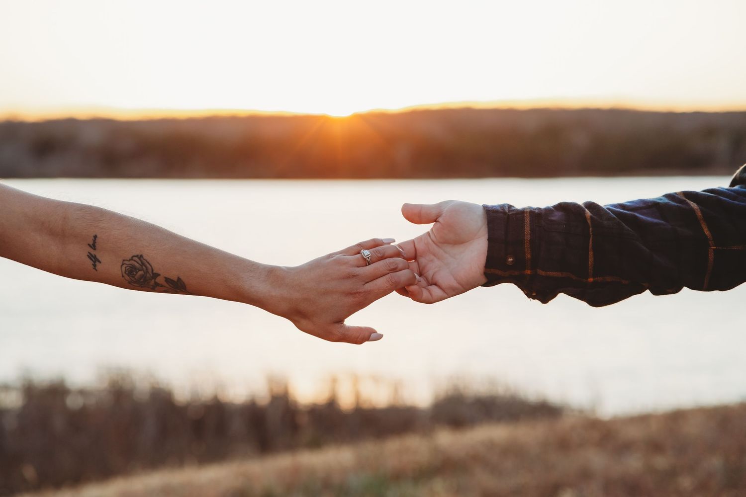 man and woman, reaching to each other, barley touching hands with the lake, sunset and mountains in the back ground