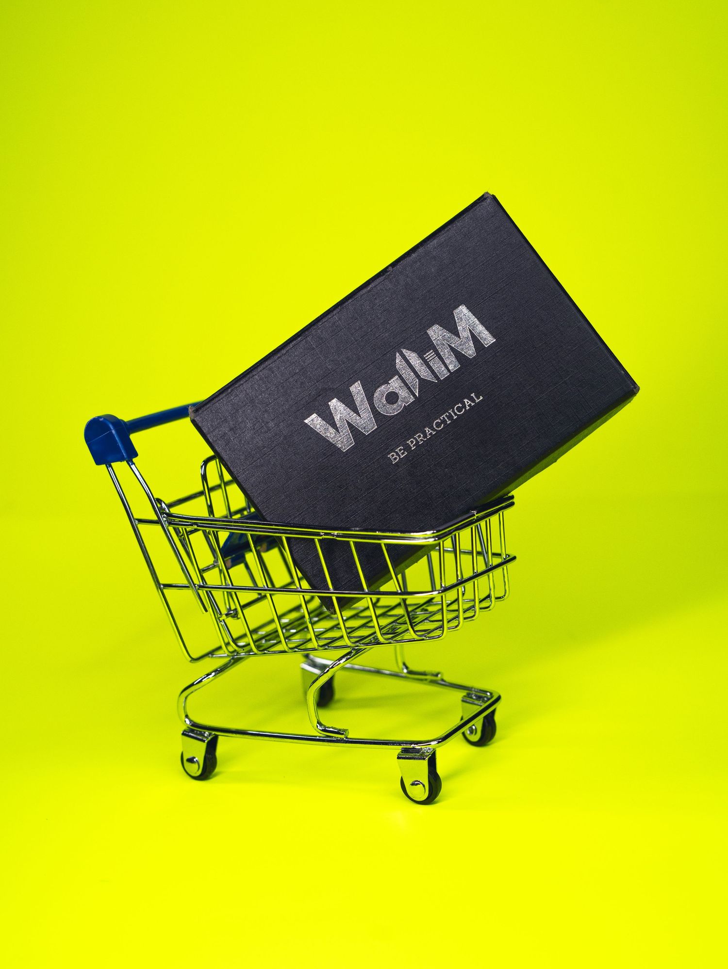 Black wallet in a miniature shopping cart against bright yellow background.