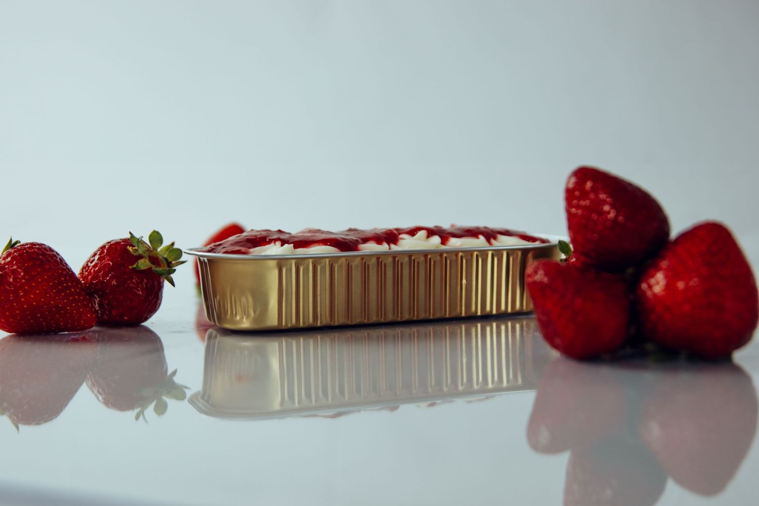 Fresh red strawberries arranged beside aluminum baking tin on white surface.