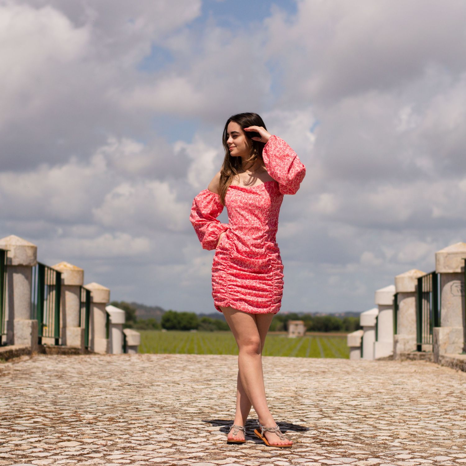Fashion model in pink outfit striking dynamic poses on stone terrace with cloudy sky backdrop.