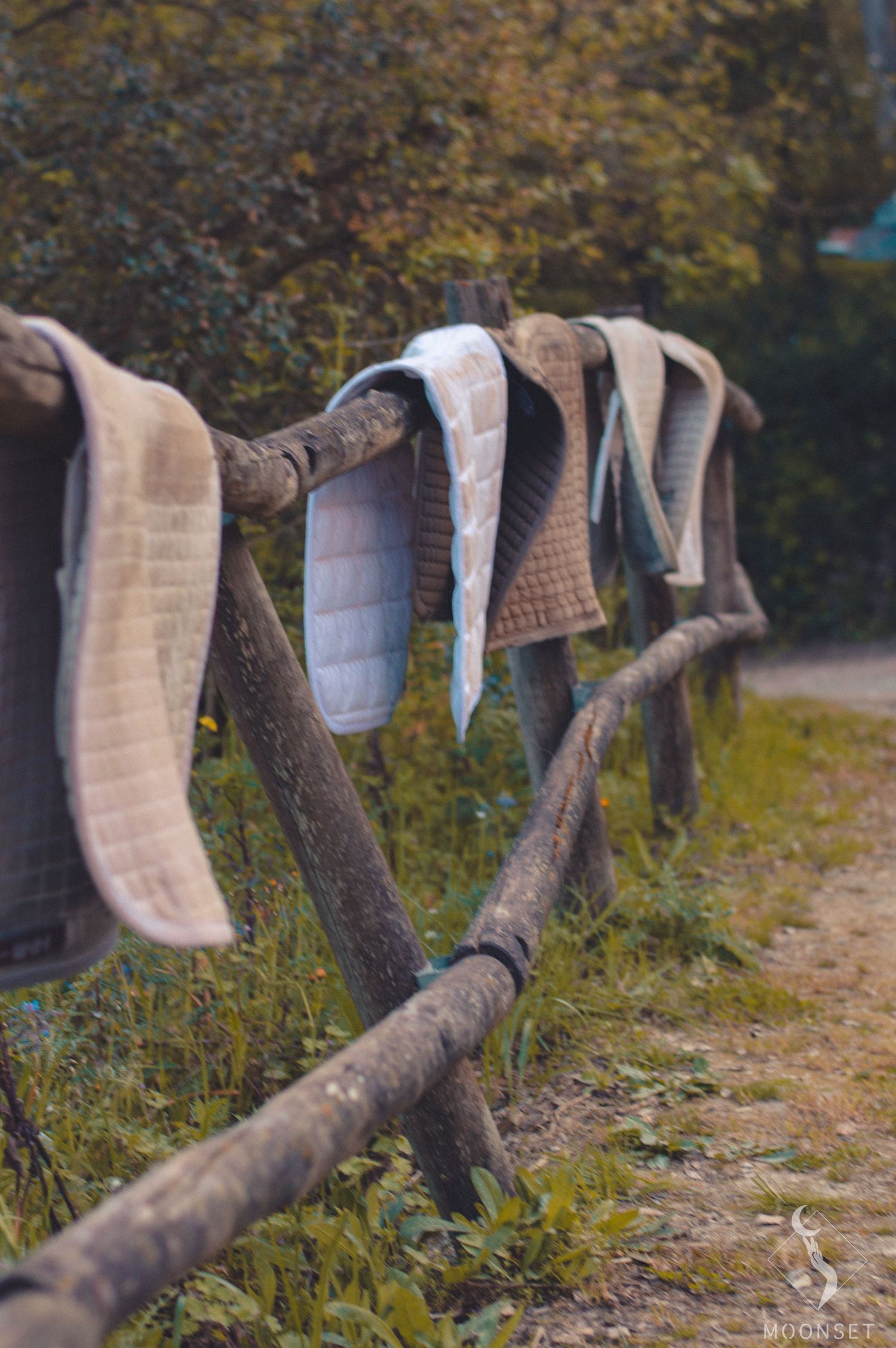 Row of saddle pads hanging to dry on wooden fence in outdoor setting.