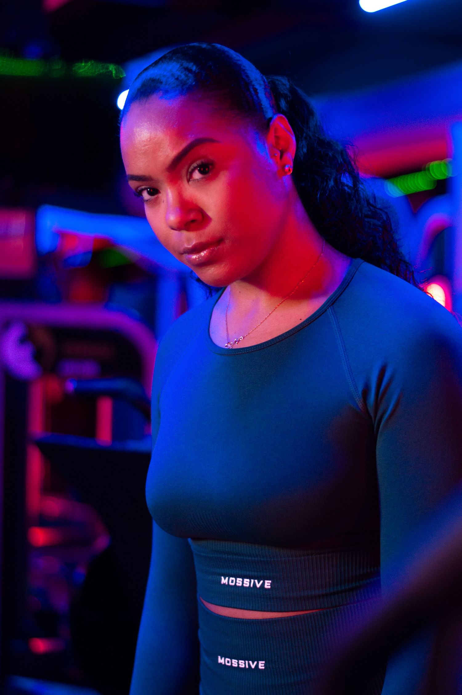 Athletic woman in dark workout attire illuminated by colorful neon lighting during fitness session.
