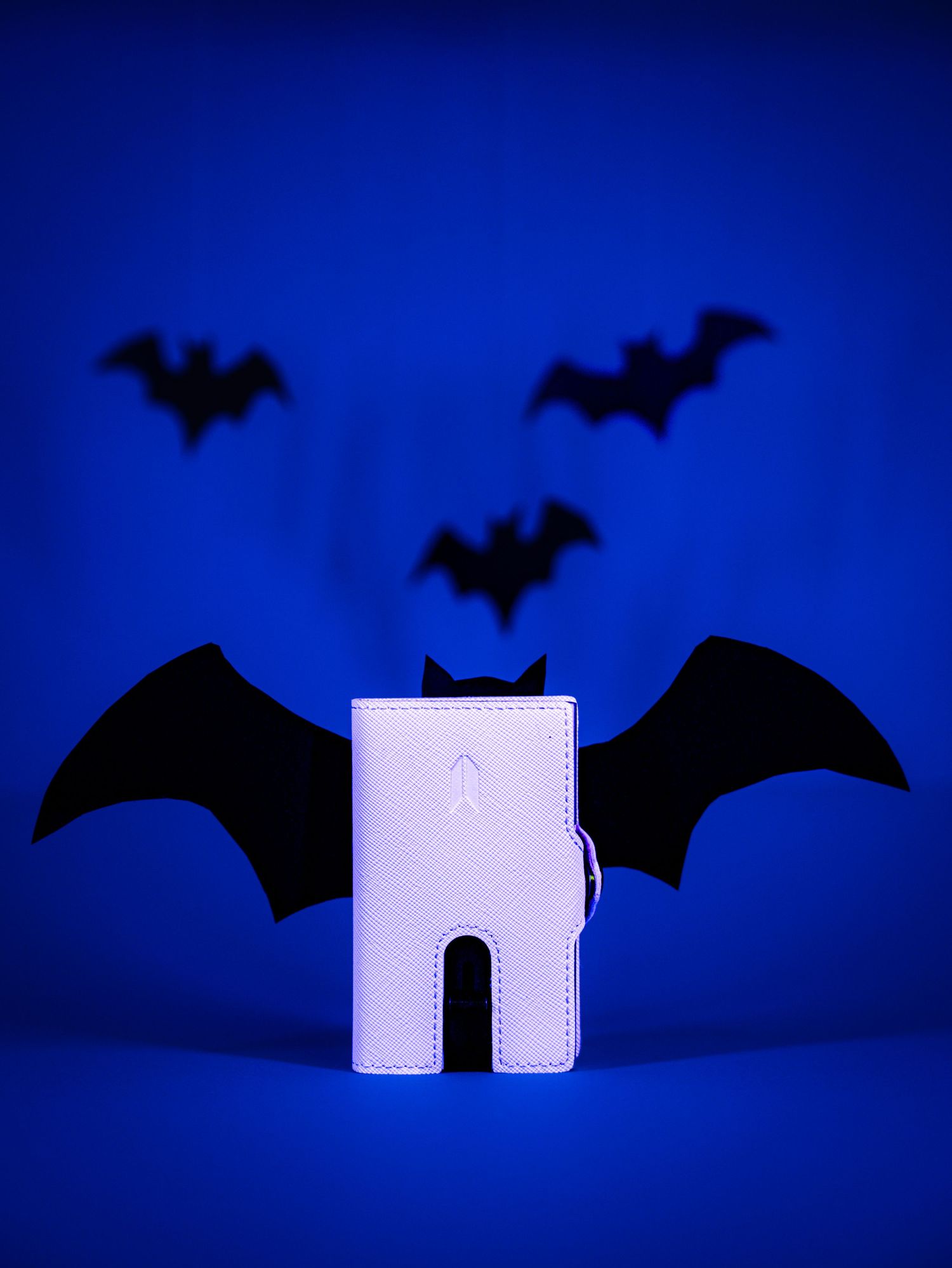 White paper cutout house with flying bat silhouettes against deep blue background.