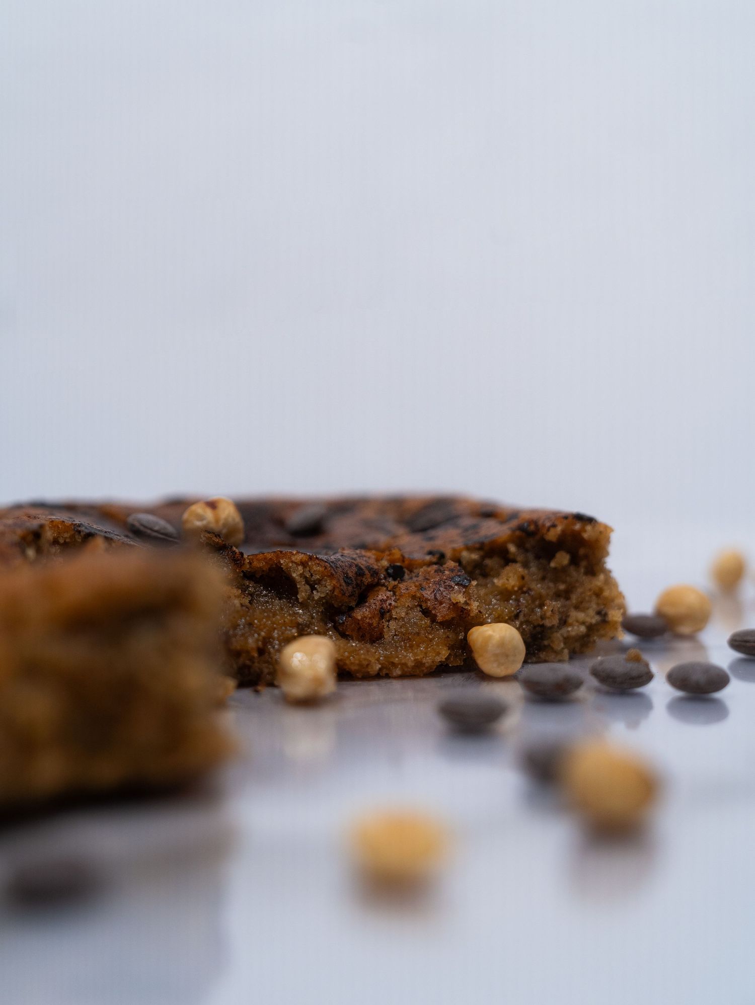 Close-up of a chocolate chip cookie bar with hazelnuts scattered around.