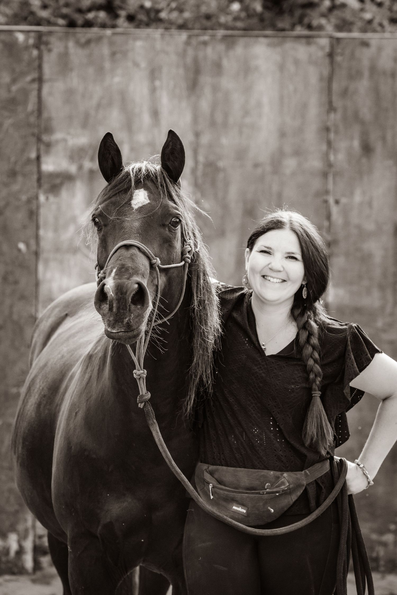 A dark horse and companion pose together against a concrete wall in black and white.