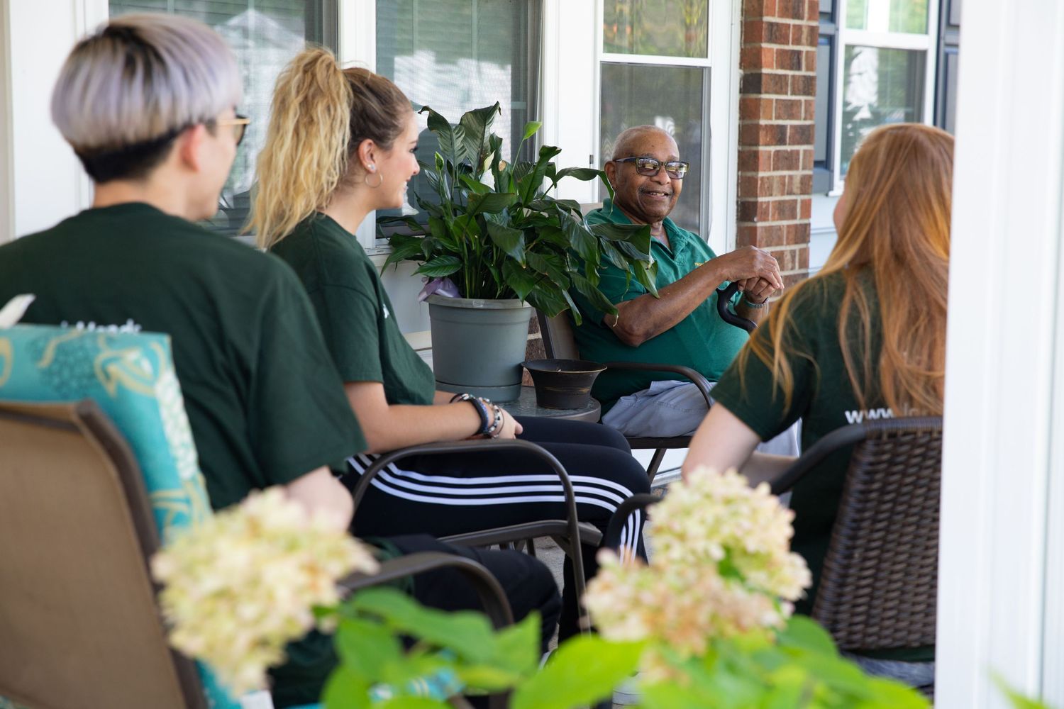 Group meeting on a porch with potted plants and outdoor furniture.