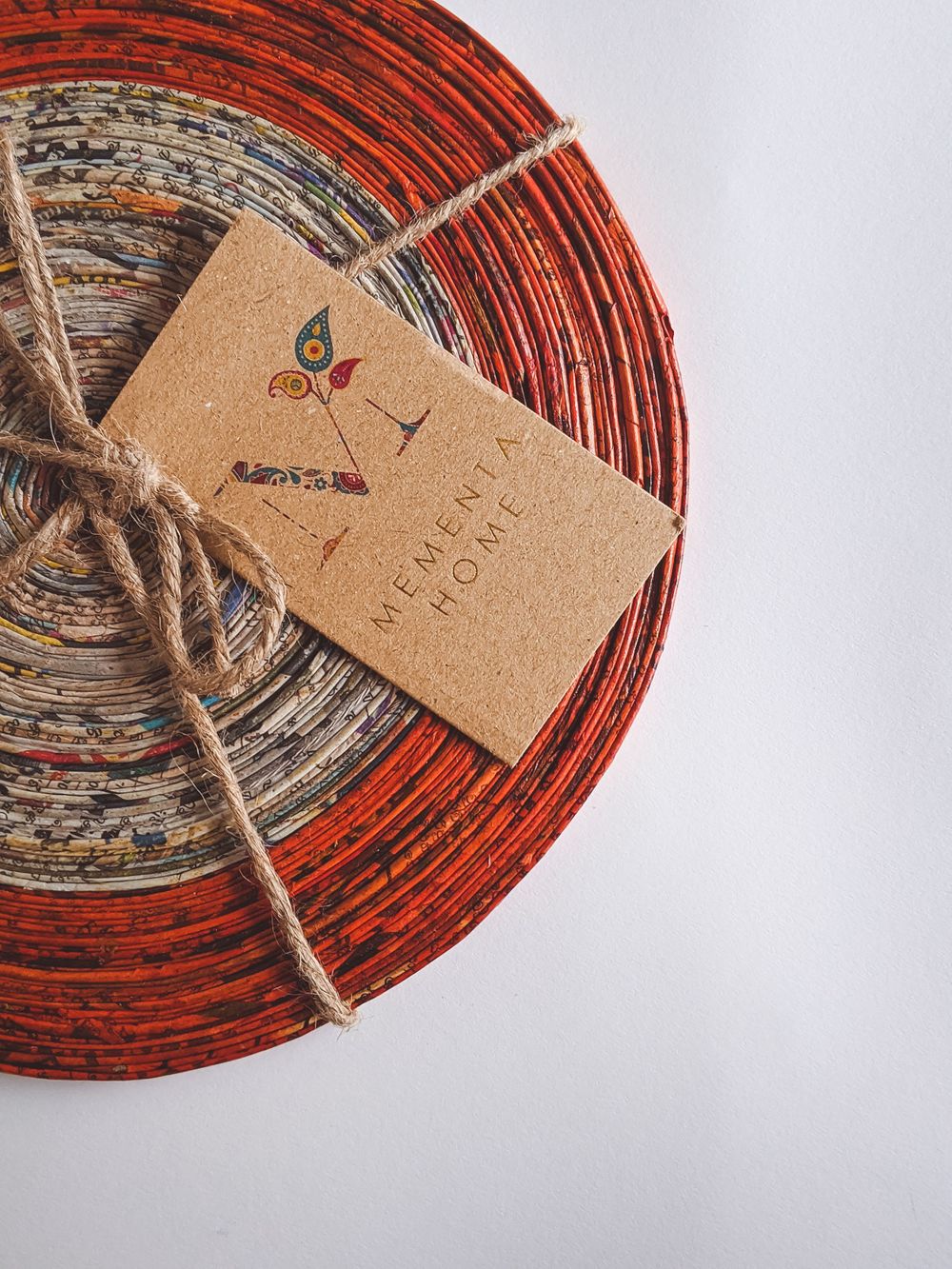 Colorful rolled paper coaster tied with twine and Memento Home kraft paper tag on white surface.