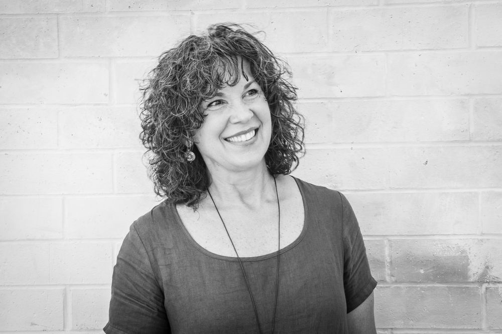 Black and white portrait of cheerful curly-haired woman smiling against a brick wall.